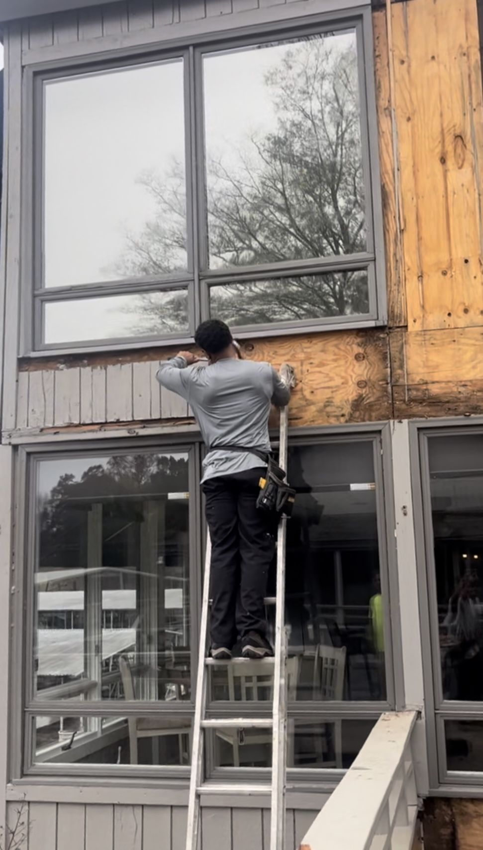 Universal Solutions crew member on a ladder removing old siding around large windows