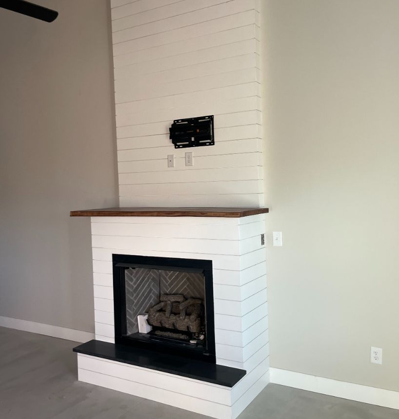 Finished fireplace with white shiplap surround, wood mantel and dark stone hearth